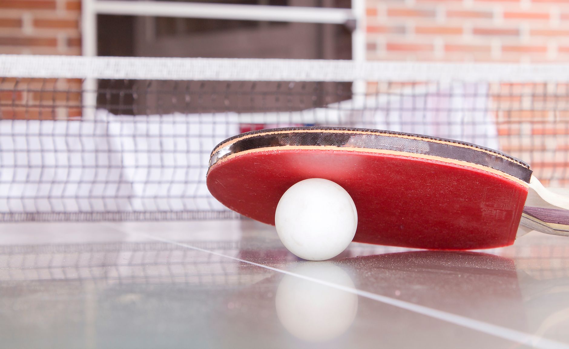 A red table tennis bat resting against a ball on the table